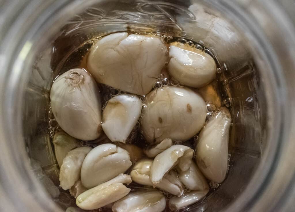 A glass jar filled with golden-hued honey infused with garlic cloves, showcasing the transformative process of fermenting garlic in honey.